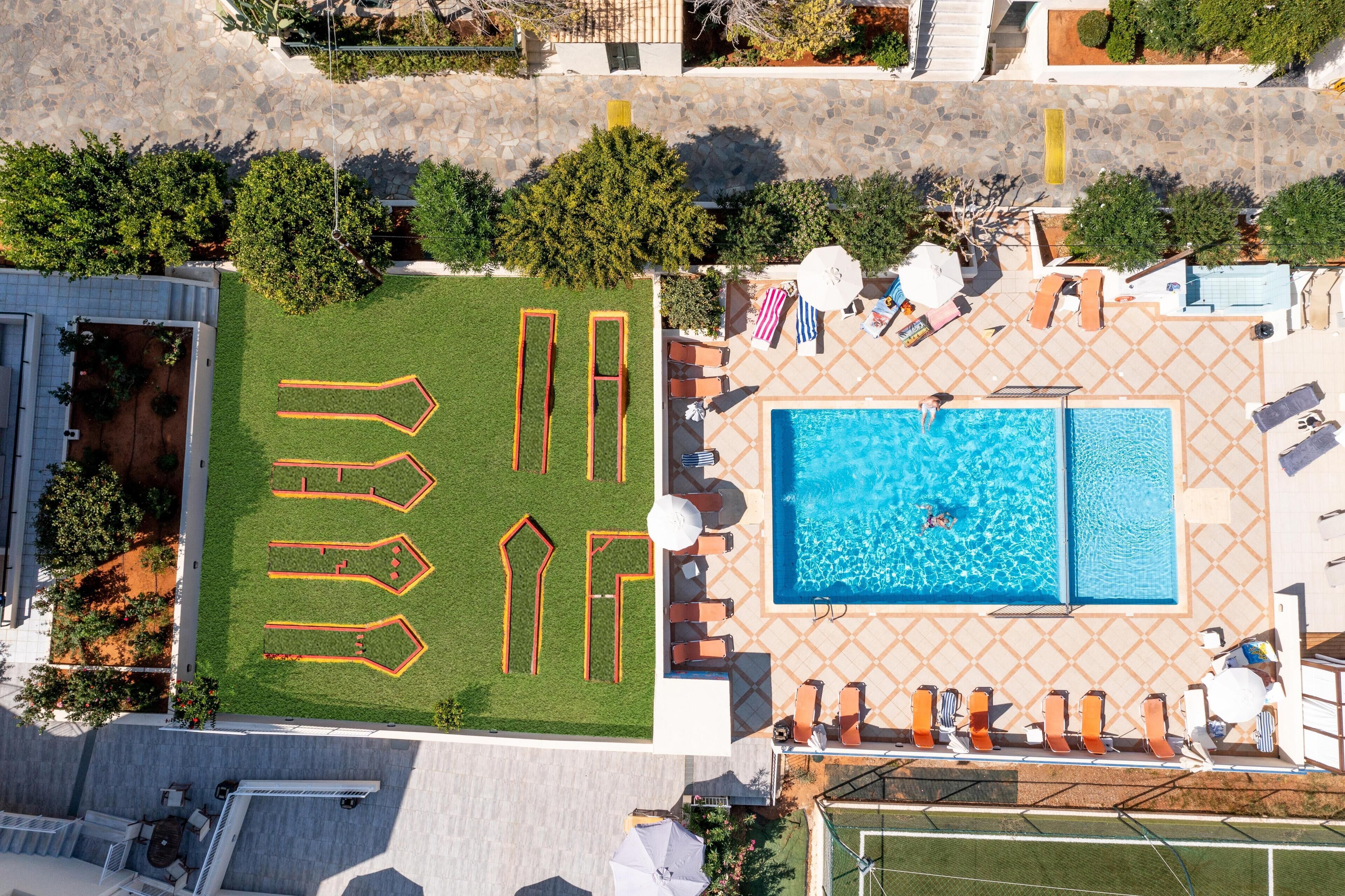 An aerial view of a property with a swimming pool, outdoor seating, and a well-maintained lawn with geometric patterns.