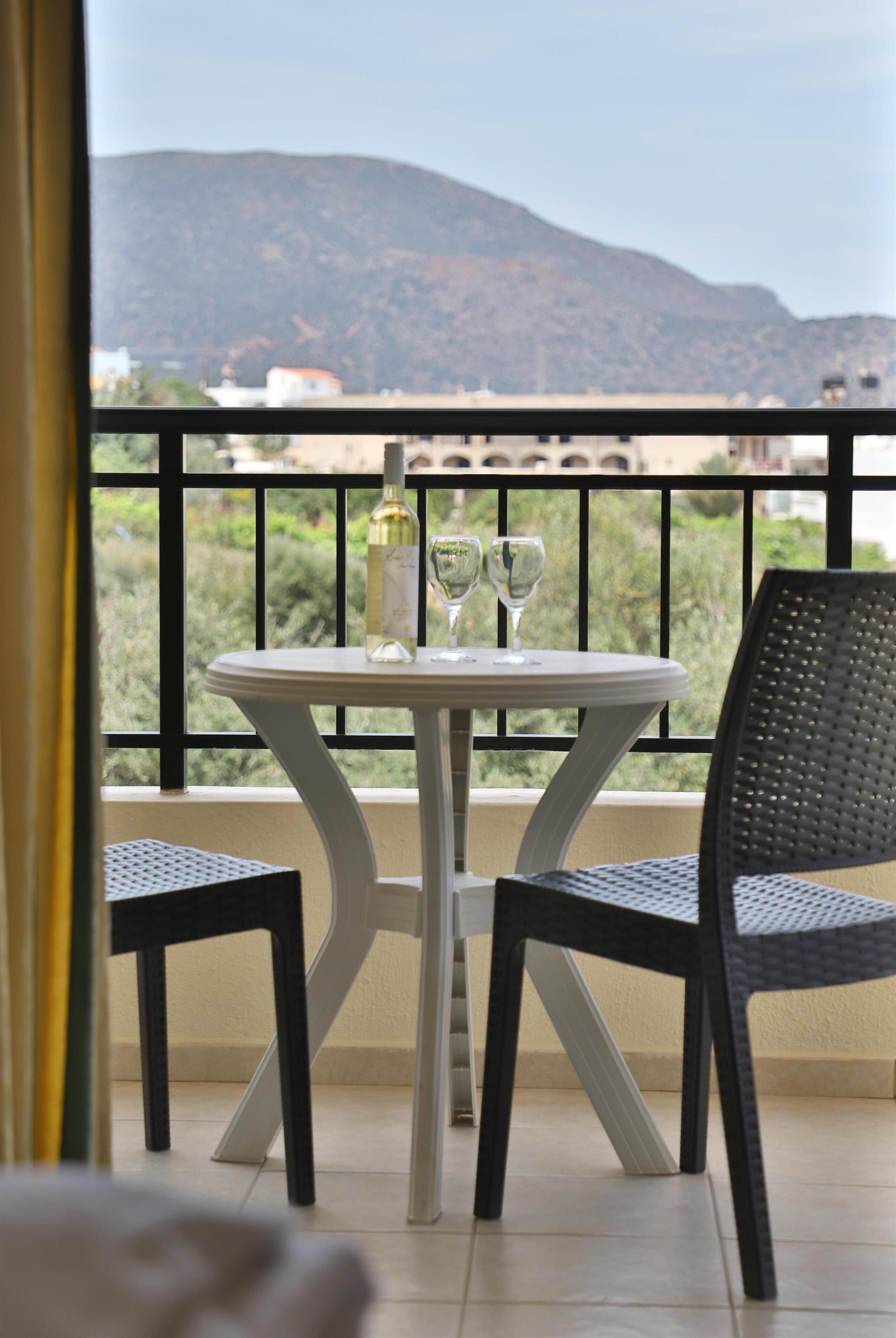 A balcony with a table and chairs, a bottle of wine, and two wine glasses.