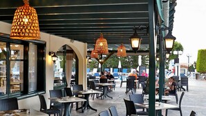 Un café al aire libre con mesas y sillas, cubierto por una pérgola con luces colgantes.