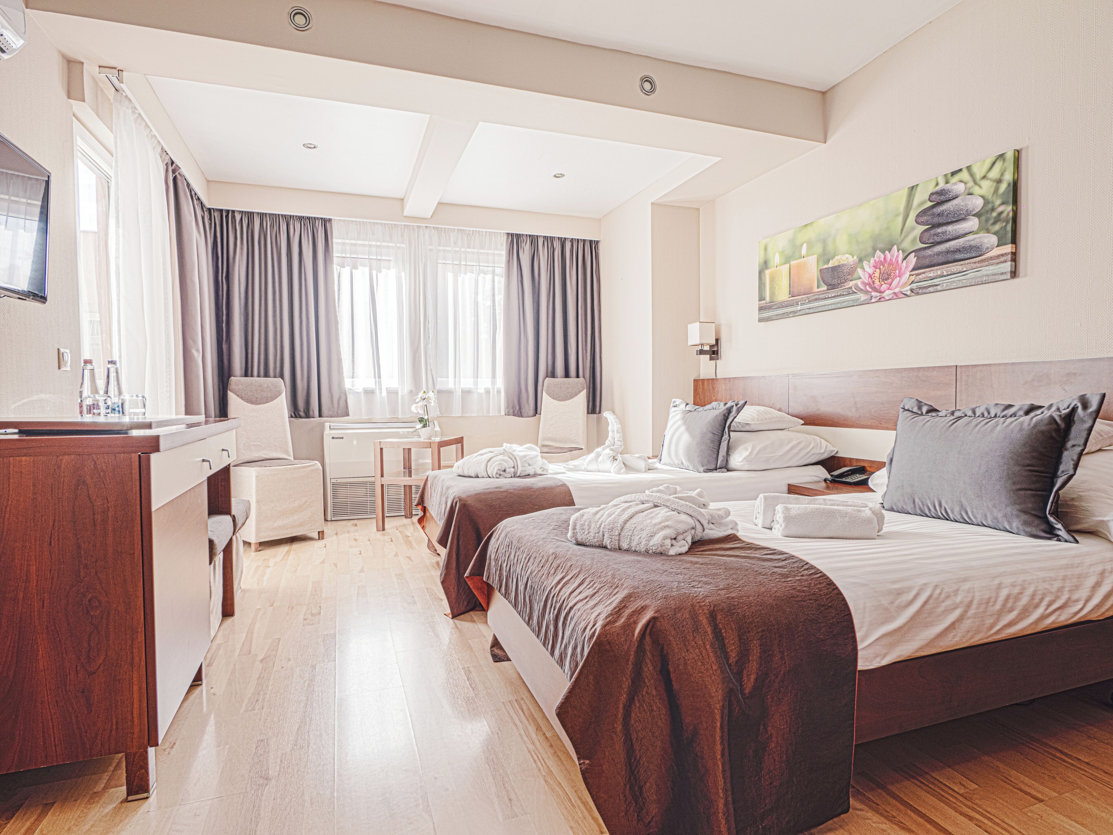 A hotel room with a bed, a desk, a chair, a TV, and a painting on the wall.