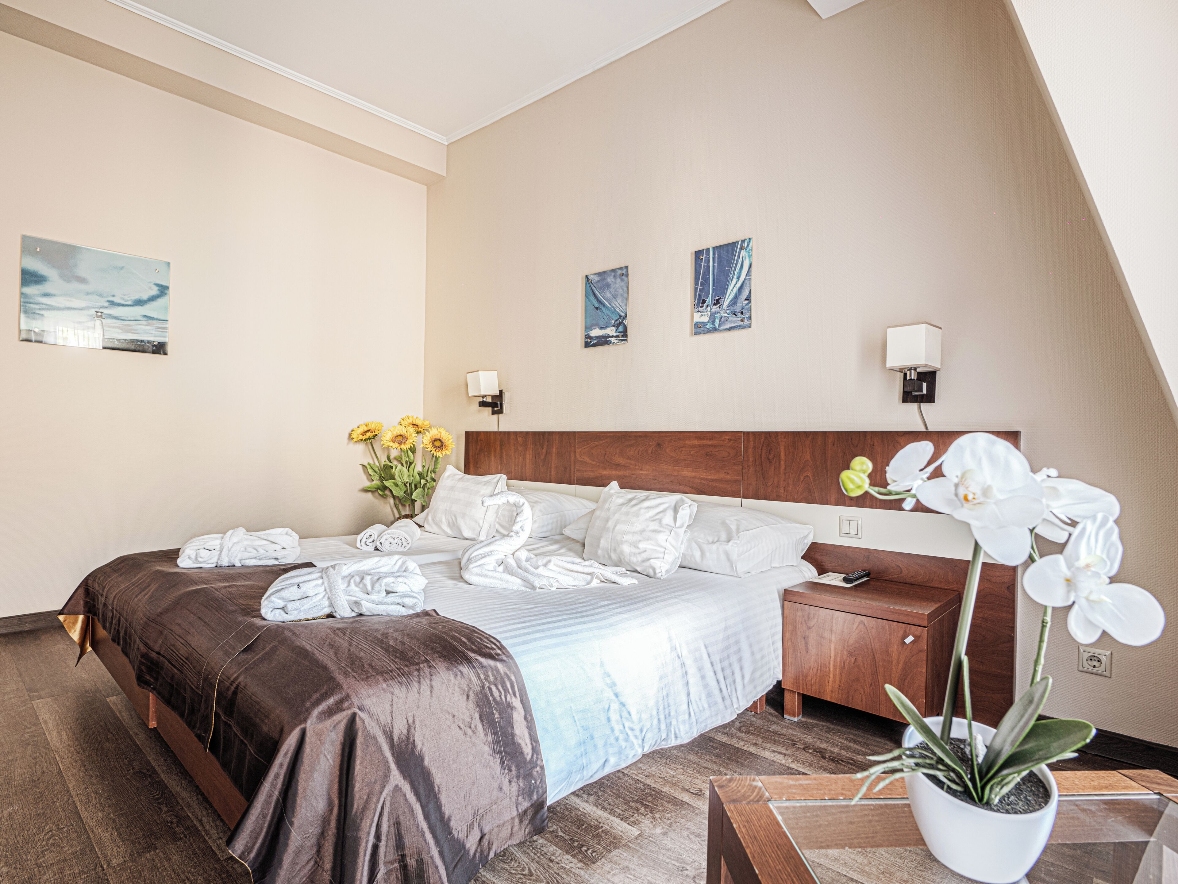 A hotel room with a bed, a nightstand, a potted orchid, and artwork on the walls.