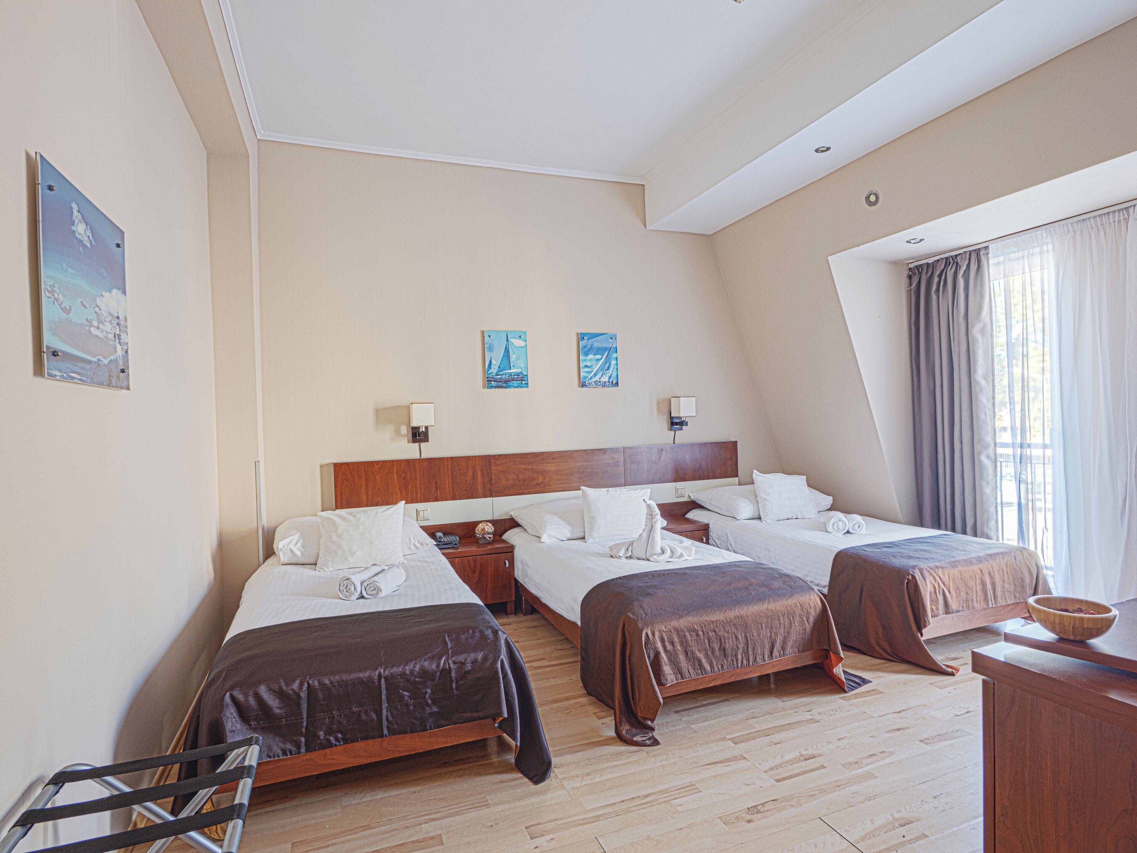 A hotel room with two beds, a wooden headboard, a desk, and a window with curtains.