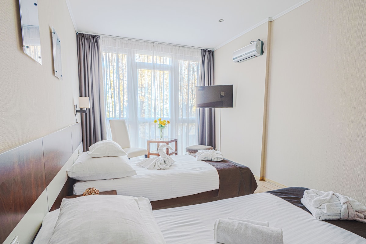 A hotel room with two beds, a TV, an air conditioner, and a window with curtains.