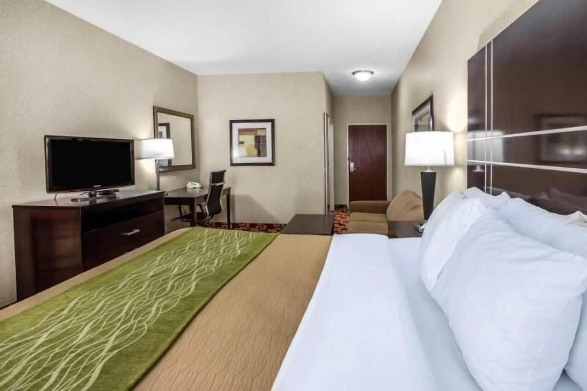 Una habitación de hotel con cama, escritorio con televisor, una silla, lámpara y puerta.