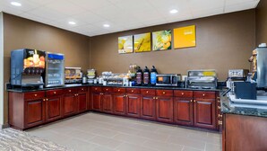 Una cocina de hotel con barra de desayuno tipo autoservicio, una máquina de café y un microondas.