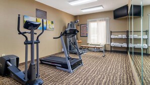 Un gimnasio de hotel con equipo de ejercicio, un televisor y una ventana con cortinas.