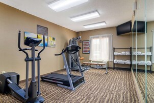 Un gimnasio de hotel con equipo de ejercicio, un televisor y una ventana con cortinas.