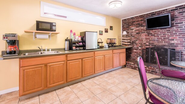 A kitchen with wooden cabinets, a microwave, a coffee maker, and a brick wall with a TV. - Relax Inn (Brunswick)