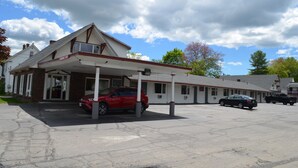 A motel with a covered parking area, a red car parked in front, and a black truck parked in the background. - Relax Inn (Brunswick)