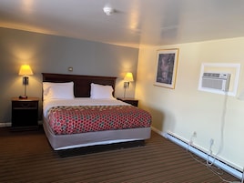 Habitación de hotel con cama, dos lámparas de noche, aire acondicionado montado en la pared y un cuadro enmarco.