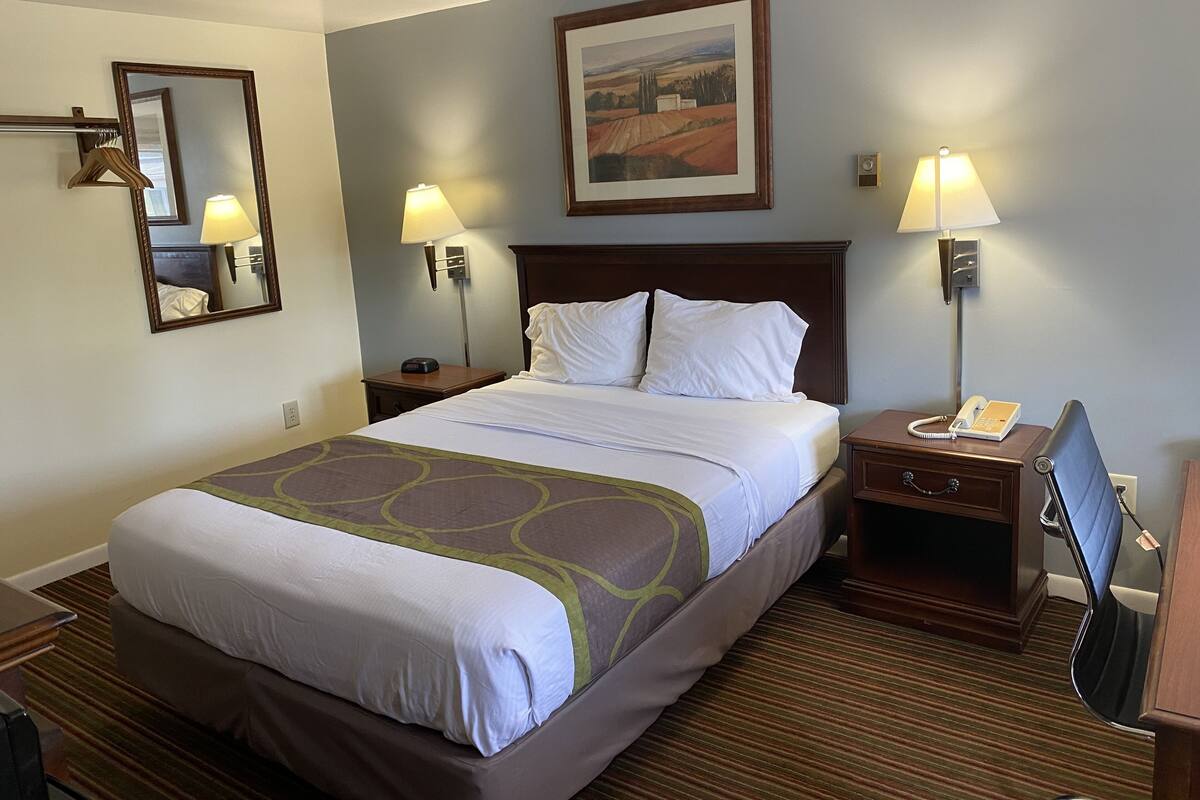 A hotel room with a large bed, two bedside tables with lamps, a desk with a chair, a mirror, and a framed picture on the wall.