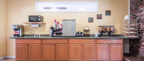 A kitchen with a central island, wooden cabinets, a microwave, a refrigerator, and various kitchen appliances.
