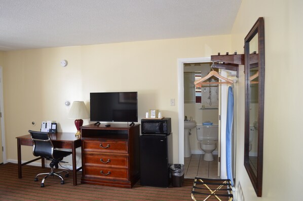 A hotel room with a desk, chair, dresser, television, microwave, and a bathroom visible through an open door. - Relax Inn (Brunswick)