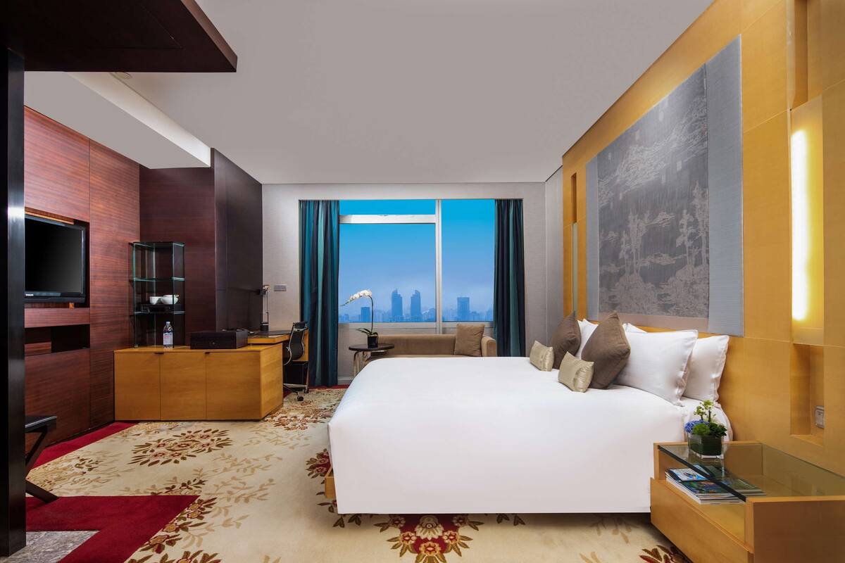 Une chambre d’hôtel moderne dotée d’un grand lit, d’une télévision, d’un bureau et offrant une vue sur le panorama urbain.