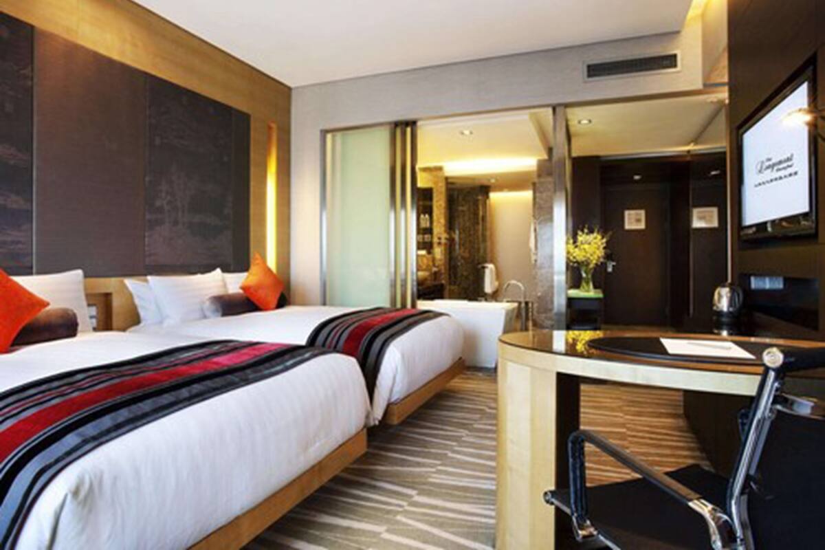 Une chambre d’hôtel avec deux lits, un bureau et une salle de bain visible à travers une porte en verre.
