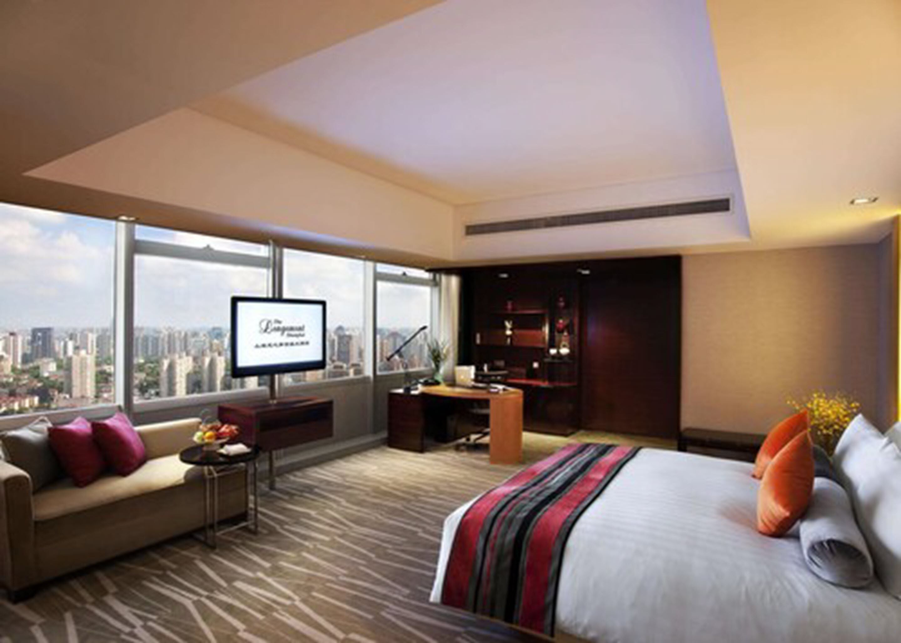 A modern hotel room with a large bed, a sofa, a desk, and a TV.