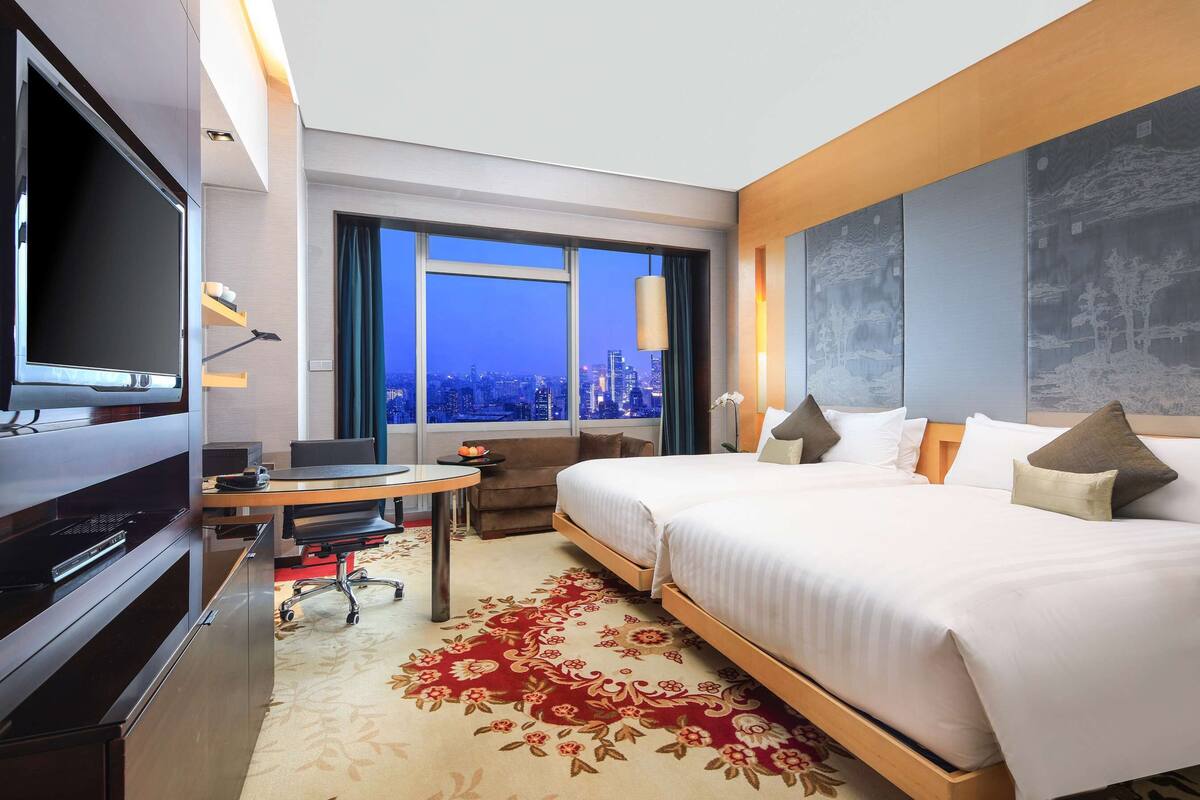Une chambre d’hôtel avec un grand lit, un bureau avec un ordinateur, une télévision et une vue sur la ville.