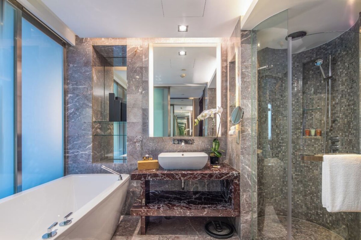 Un baño moderno con tocador de mármol, bañera independiente y zona de ducha con mampara de vidrio.