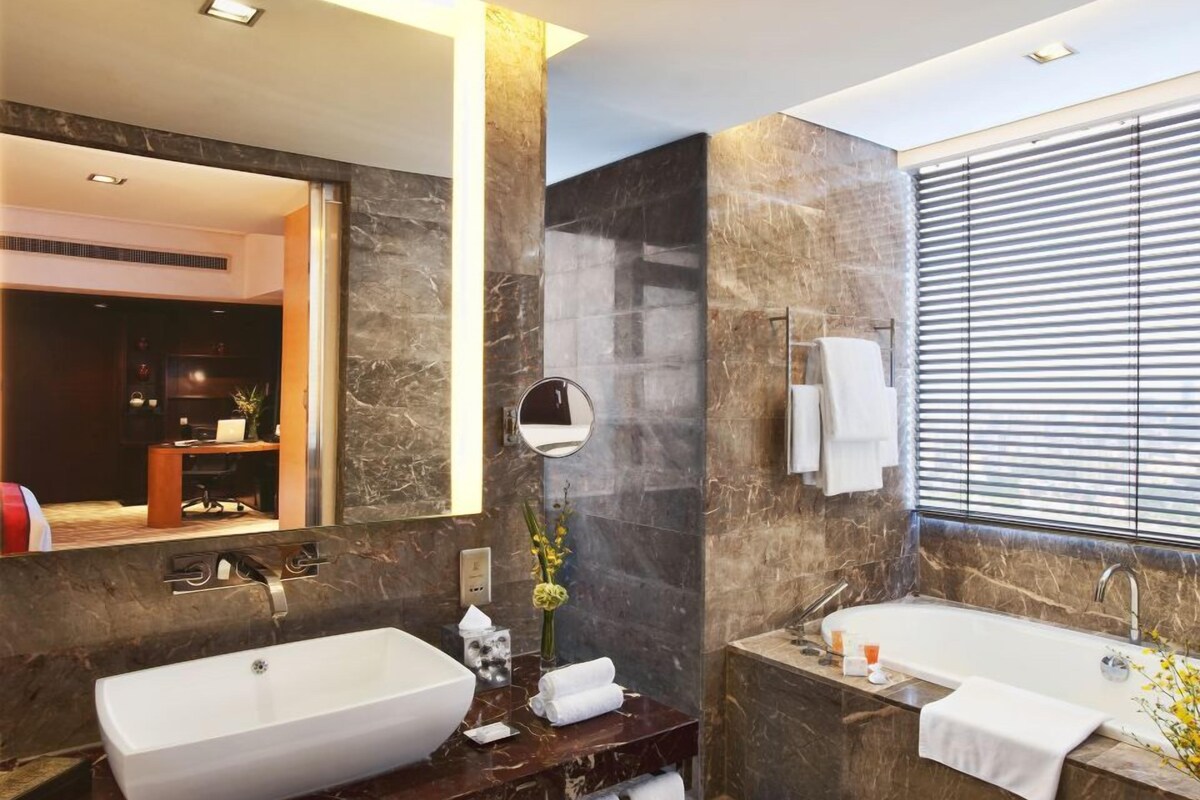 A modern bathroom with two sinks, a large mirror, and a window with blinds.