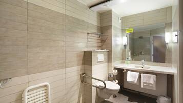 Un baño moderno con baldosas color beige, un inodoro blanco, un lavabo con espejo y un perchero para toallas.