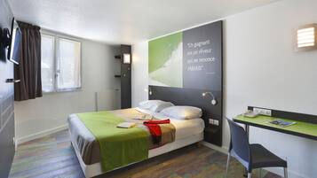 A modern hotel room with a bed, a desk, and a motivational quote on the wall.
