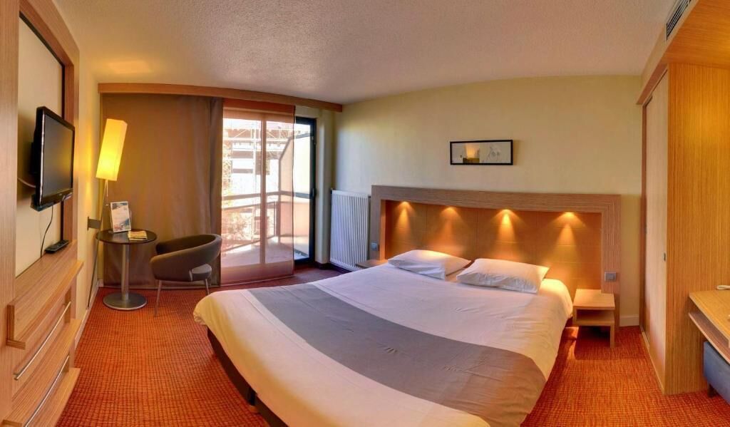 A hotel room with a large bed, a desk, a chair, a television, and a window with a view.