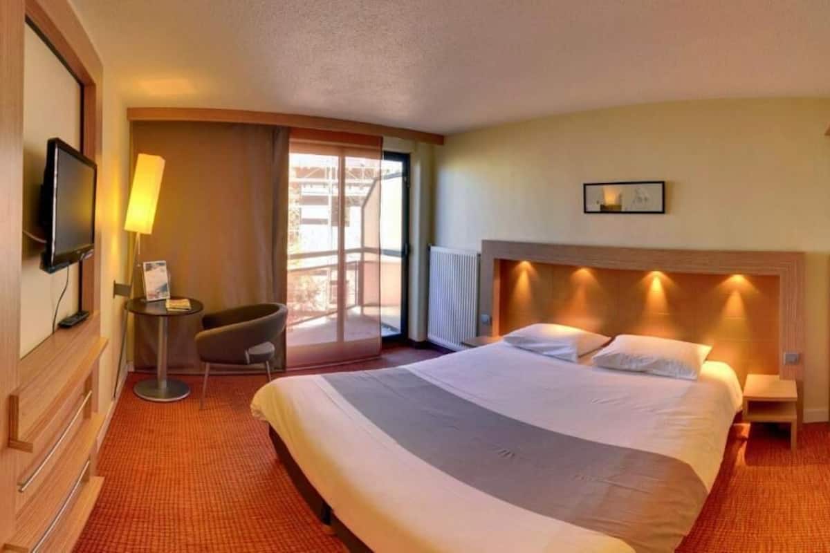 Ein Hotelzimmer mit einem großen Bett, einem Schreibtisch, einem Sessel, einem Fernseher und einem Fenster mit Blick.
