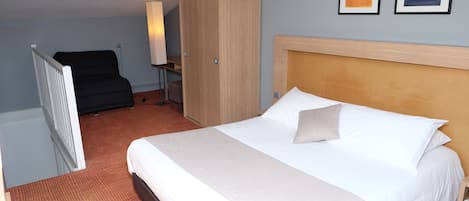 A hotel room with a large bed, a wardrobe, a desk, and two framed artworks on the wall.