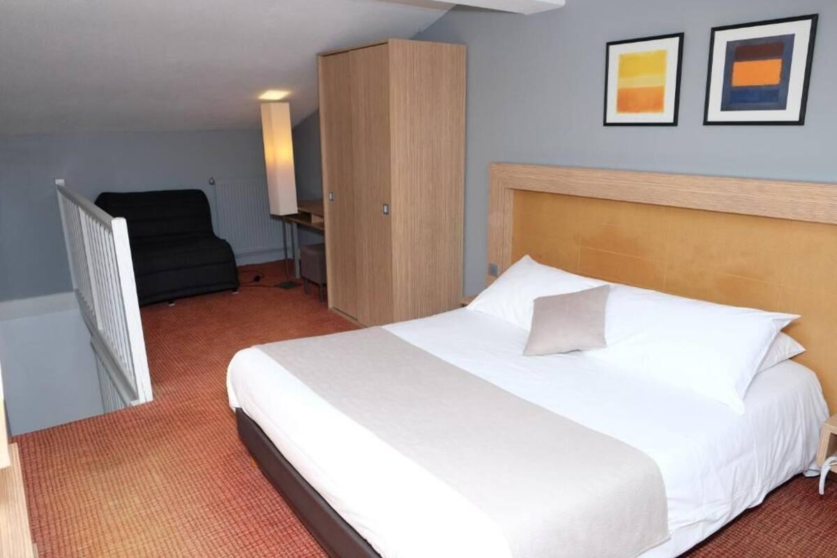 A hotel room with a large bed, a wardrobe, a desk, and a chair.