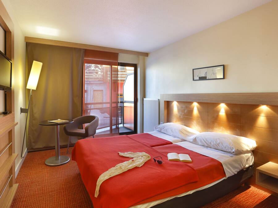 Une chambre d’hôtel avec un grand lit, un bureau, une chaise, une télévision et un balcon.