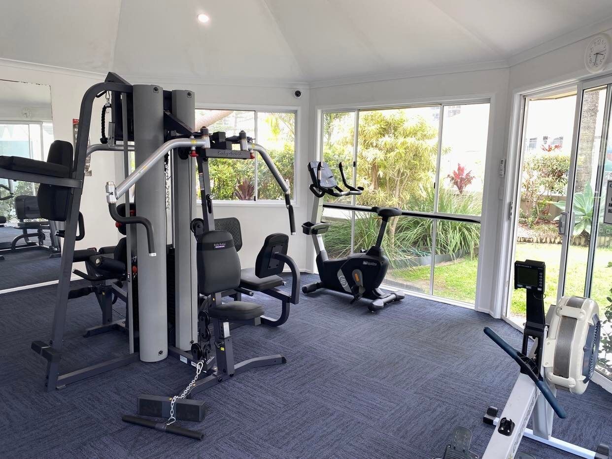 Un gimnasio con máquinas de cardio, equipo de levantamiento de pesas y un amplio ventanal con vistas al exterior.