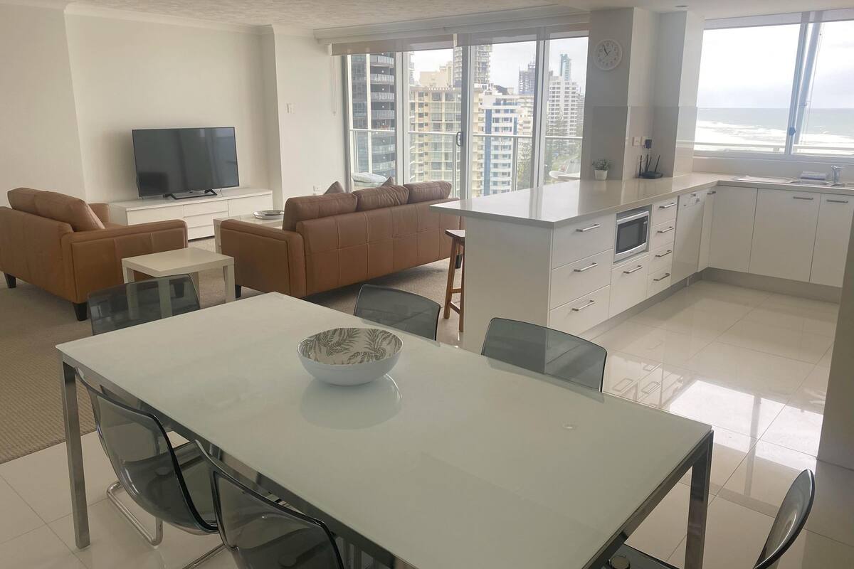 A modern living room with a sofa, a TV, and a dining area with a table and chairs.