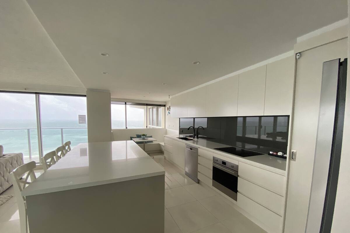 A modern kitchen with a large island, white cabinetry, and a view of the ocean.