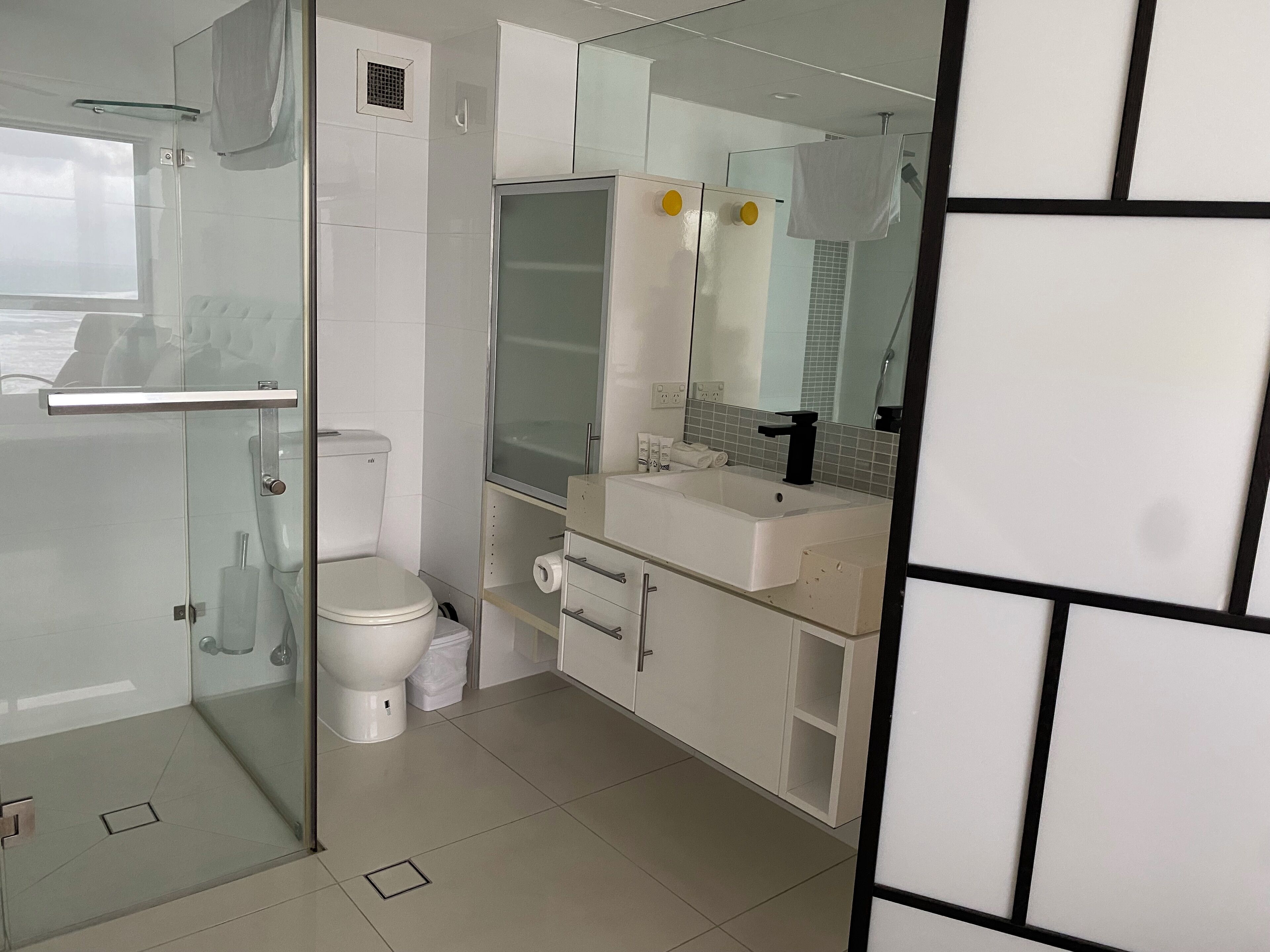 Un baño moderno con cabina de ducha de vidrio, inodoro blanco, lavabo con espejo y un mueble.