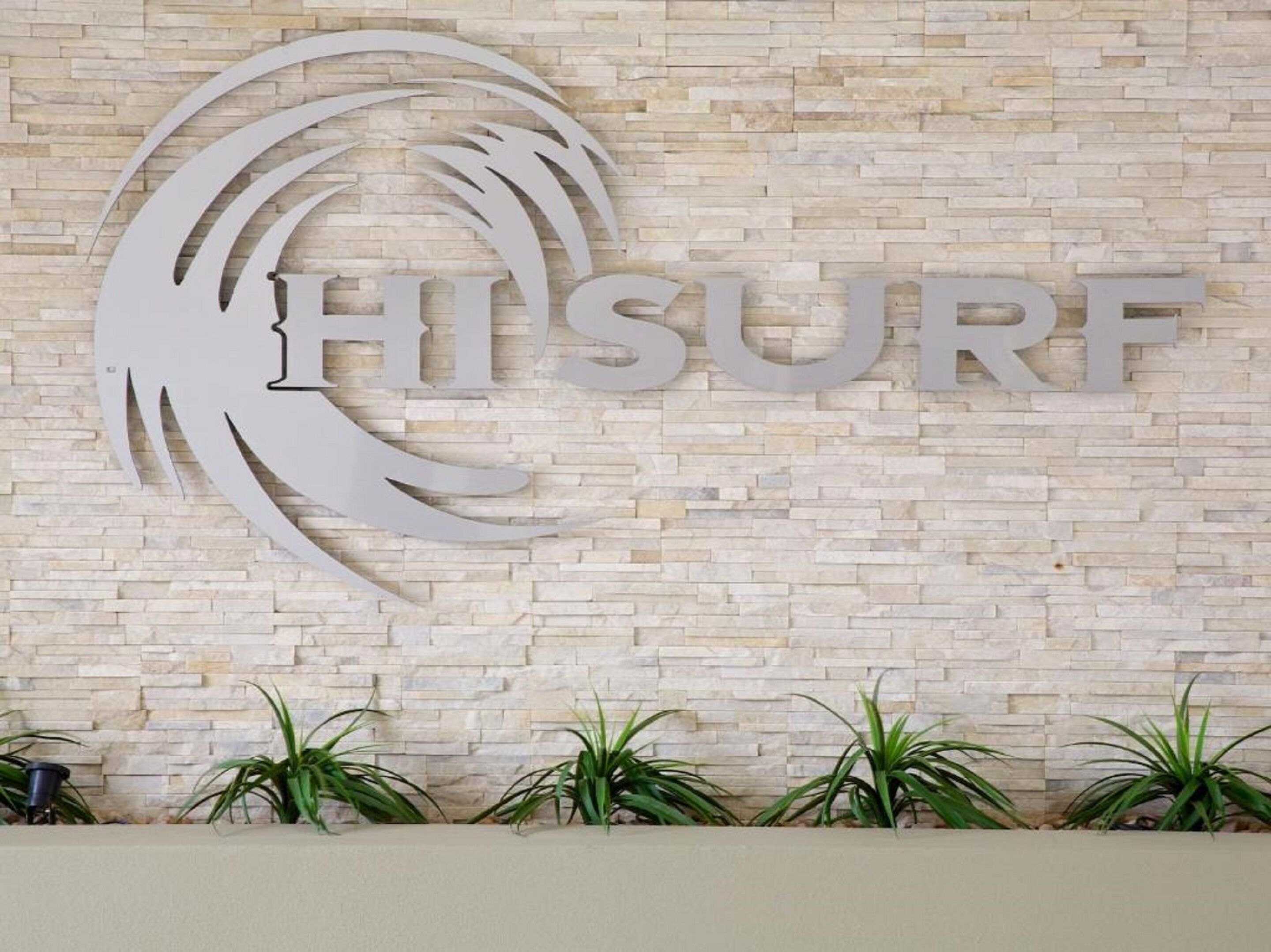 A sign with the word "HISURF" on a stone wall, surrounded by potted plants.