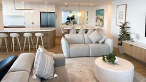 A modern living room with a grey sofa, a round coffee table, and a dining area with a wooden table and chairs.