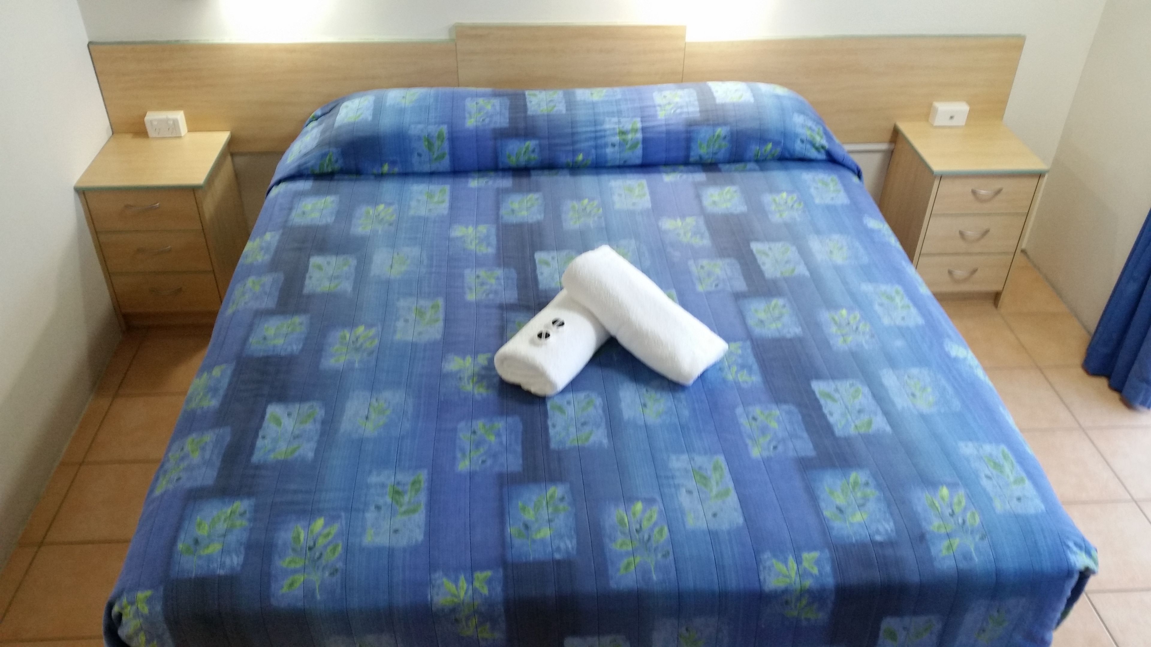 Una cama con colcha azul estampada, dos mesitas de noche y un cabecero de madera.