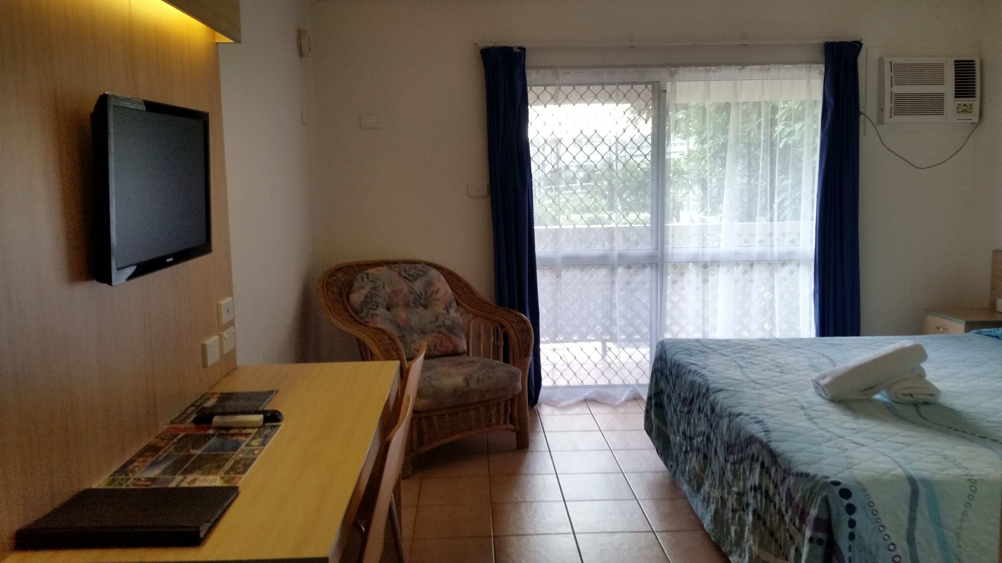 Una habitación de hotel con una cama, una silla, una mesa con una revista y un televisor en la pared.
