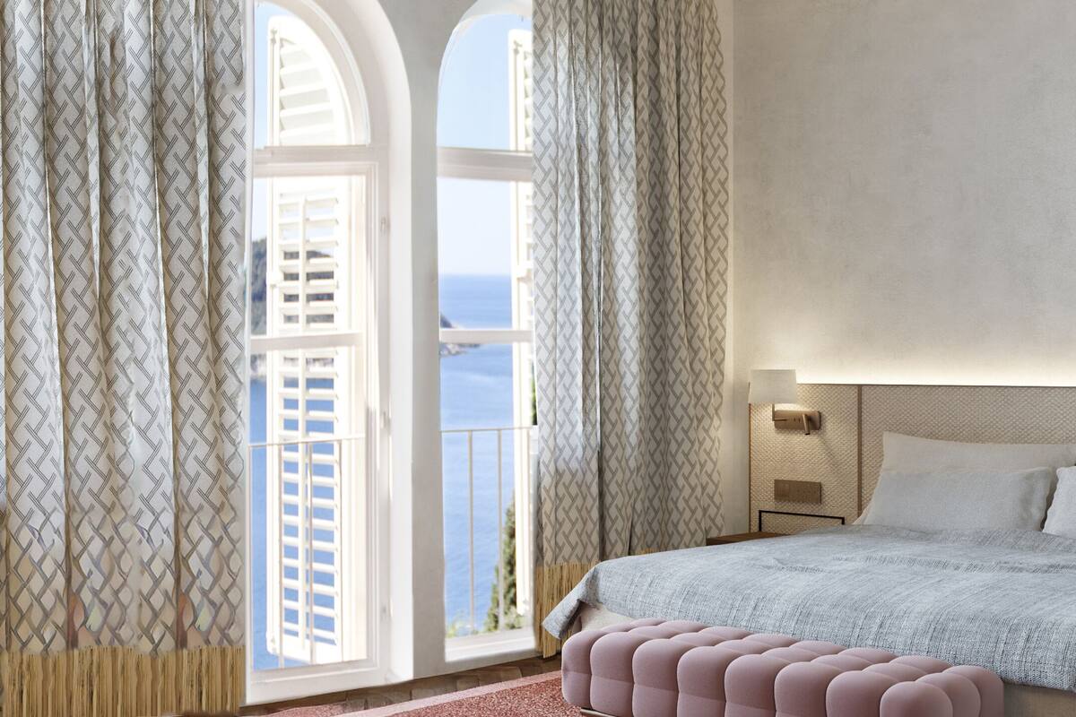 Ein Schlafzimmer mit großem Fenster, einem Bett, einem Nachttisch und Blick aufs Meer.