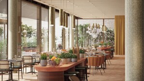 Un restaurante moderno con una barra larga, varias mesas y sillas. Hay plantas en macetas y una lámpara decorativa.