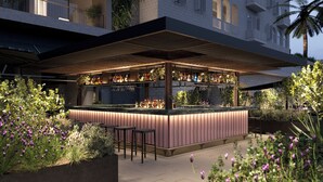 Un área de bar al aire libre con mostrador, taburetes y una variedad de botellas y vasos.