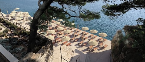 A seaside terrace with rows of sun loungers and umbrellas, overlooking a calm sea.