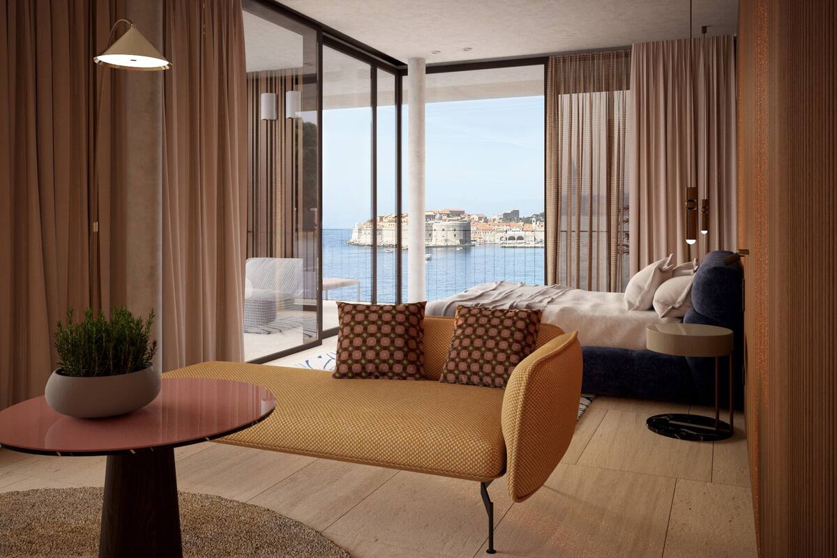 Ein modernes Hotelzimmer mit einem großen Balkon, einer Couch, einem runden Tisch mit einer Pflanze und Blick auf eine Küstenstadt.