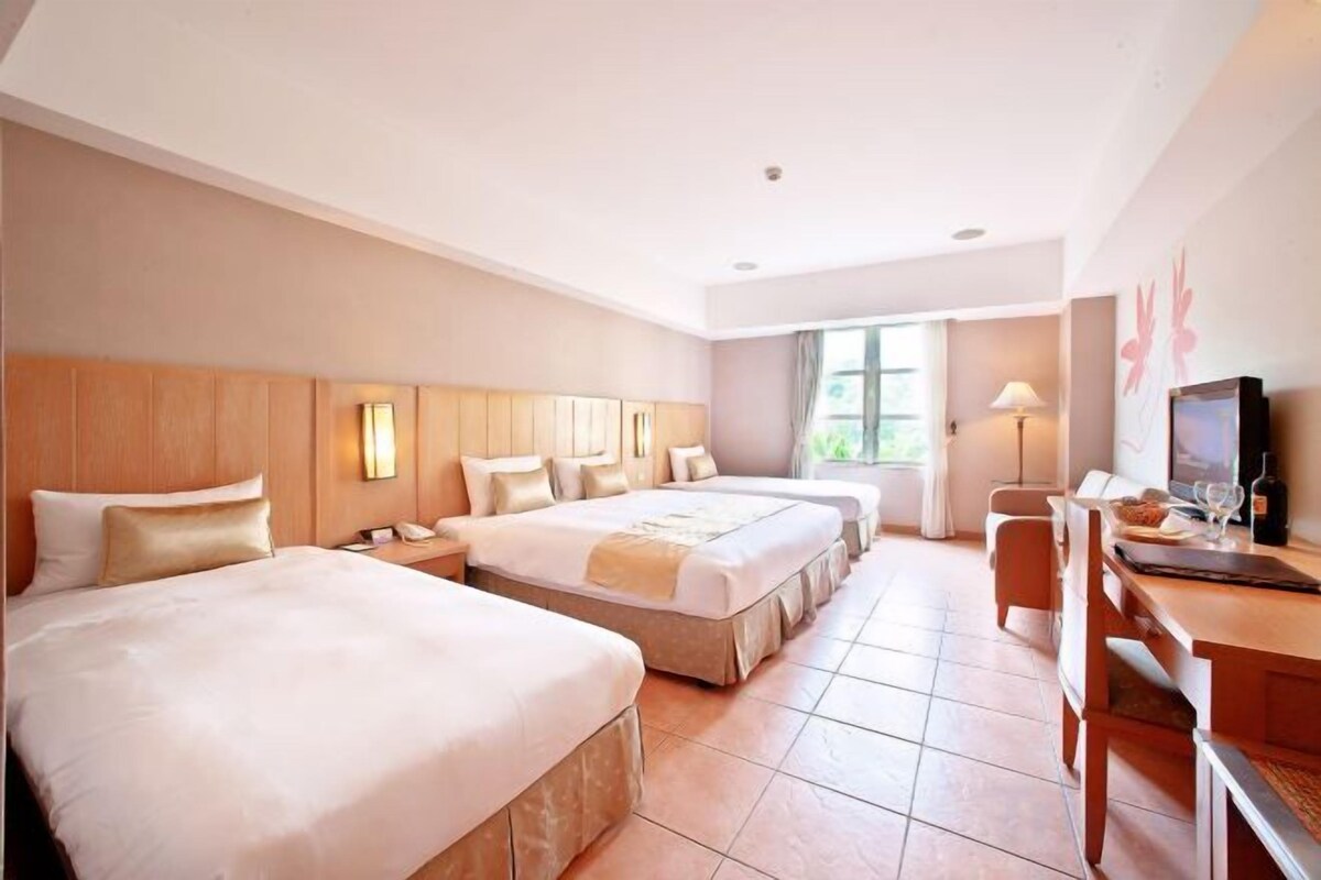 A hotel room with two beds, a desk, a chair, a TV, and a window.