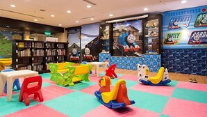 Zona de juegos infantiles con un mural de Thomas el Tren, una estantería y coloridos tapetes de juego.