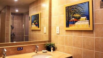 A bathroom with a large mirror, a sink, and a shower. There are two framed paintings on the wall.
