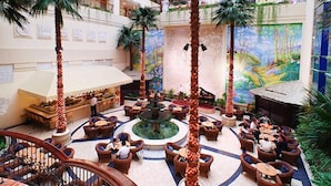 Un vestíbulo de hotel con una fuente central, varias zonas de estar y un mural en la pared.