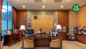 Een hotel receptie met een houten toonbank, twee stoelen, een televisie, een kleine kerstboom en een klok aan de muur.