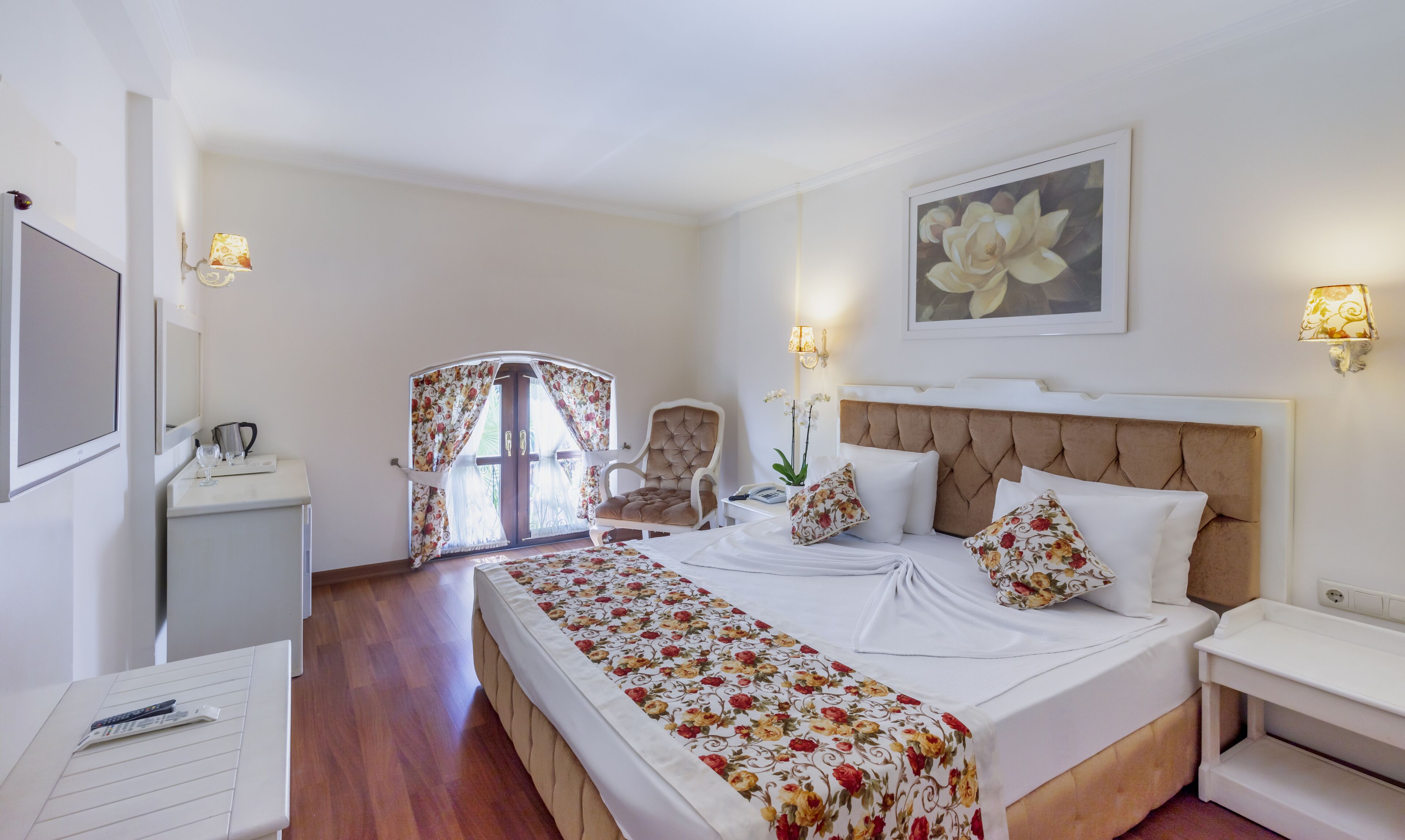 A hotel room with a bed, a chair, a desk, a lamp, and a painting on the wall.