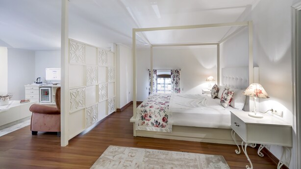 A bedroom with a four-poster bed, a bedside table with a lamp, and a desk with a computer. - Adalya Port Hotel (Antalya)